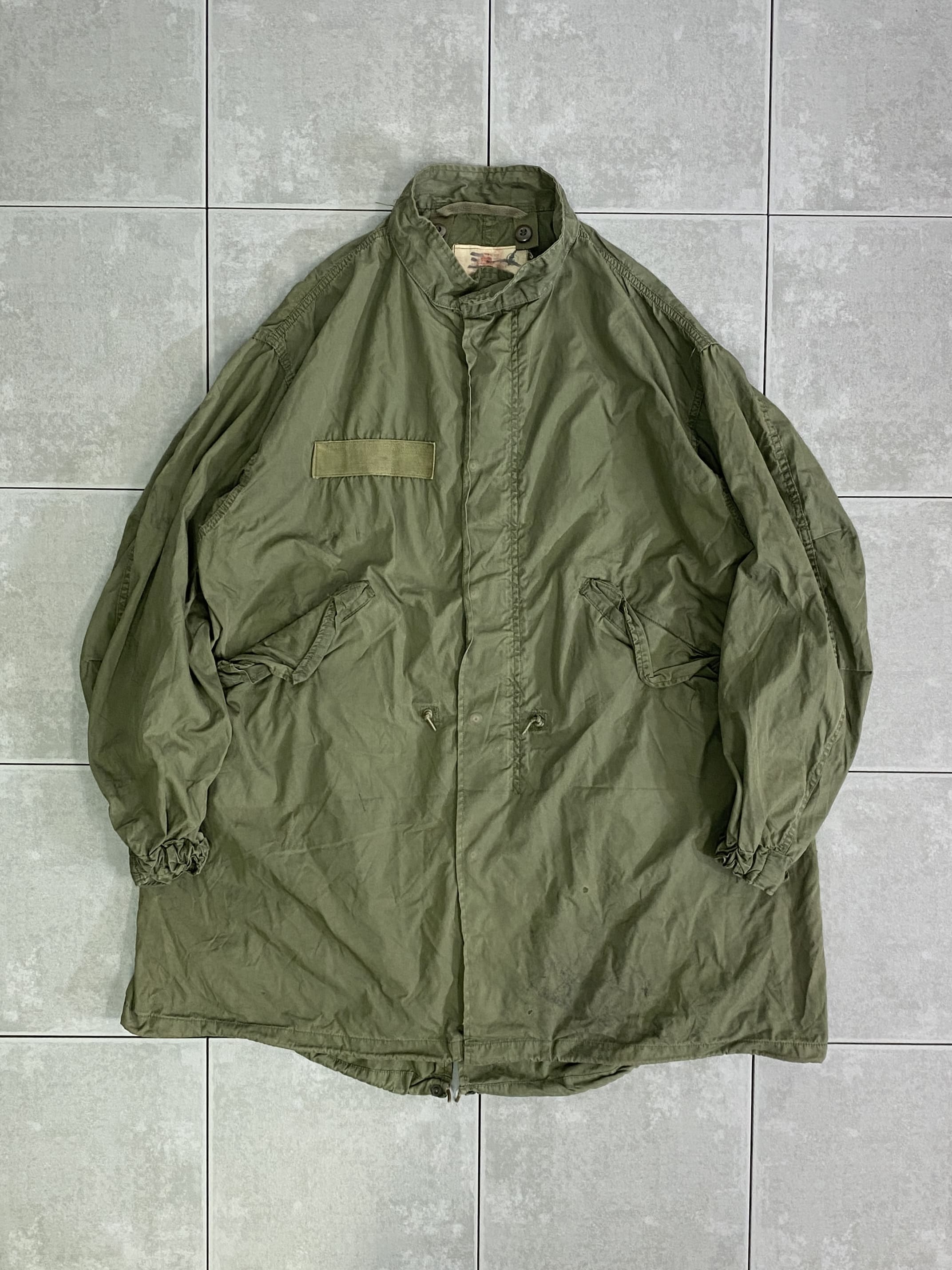 米軍放出品 実物

PARKA EXTREME COLD WEATHER M-65 PARKA 

カラー：OD

サイズ：M-R
着丈：約96cm　身幅：約72cm　肩幅：約61cm　袖丈：約61cm

素材：コットン　ナイロン

1960年代後半からアメリカ地上軍に採用された
65年型極寒用野戦パーカー。

フラップの付いた大型のハンドポケット、フィッシュテール型の裾など、
基本的には前モデルのM-51パーカーを引き継ぐ形です。

M-51パーカーでは縫い付けであったフードが
M-65では脱着式に変更、肩のエポレットが省略されており、
裾のドローコードがゴムに変更されております。

ヴィンテージで状態の良いものを見つけることが難しくなってきている
アイテムの一つ。

USEDのコンディションで、汚れなども見られますが
まだまだ楽しんで着用できる一枚です。

※画像の程度とは若干異なる場合がございますので予めご了承下さい。
(キズ、へこみ、汚れ、穴あき、ほつれ、文字書入れ(名前、ナンバー)など


































































































