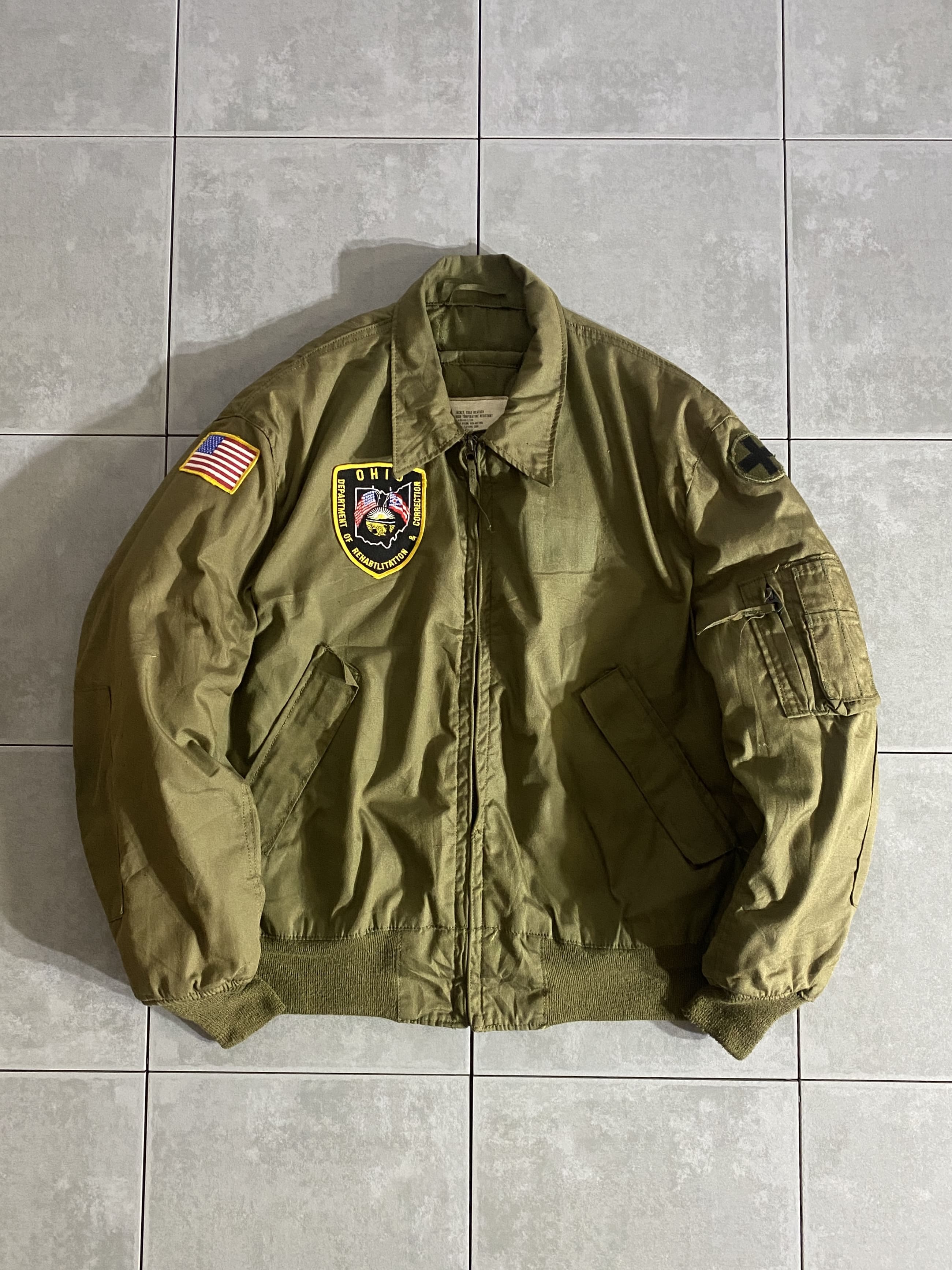 米軍放出品

80s CVC COLD WEATHER TANKERS JACKET

カラー：OLIVE

サイズ：L-L
着丈：約66cm　身幅：約61cm　肩幅：約53cm　袖丈：約61cm

素材：ナイロン100％（アラミド繊維）

SCOVILL ZIP

CVC(戦闘装甲車輌搭乗員)

軽量で耐久性に優れる難燃性素材ノーメックスを使用した
CVCのタンカースジャケット。

希少なパッチ付きです。

首もとの防寒性を高めるチンストラップや、生地を二重にして
耐久性に余裕をもたせた肘部分など、細部にわたる機能性の高さは
ミリタリーならではです。

背中に設けられたベルクロ留めの開口部は、緊急時に車輌から
乗員を引っ張り上げて救出するドラッグハンドルを引き出す為のもの。

着丈は装甲車輌に乗って邪魔にならない用に短めの
サイズ感となっており、とてもスタイリッシュな印象の一着です。

※画像の程度とは若干異なる場合がございますので予めご了承下さい。
(キズ、へこみ、汚れ、穴あき、ほつれ、文字書入れ(名前、ナンバー)など
