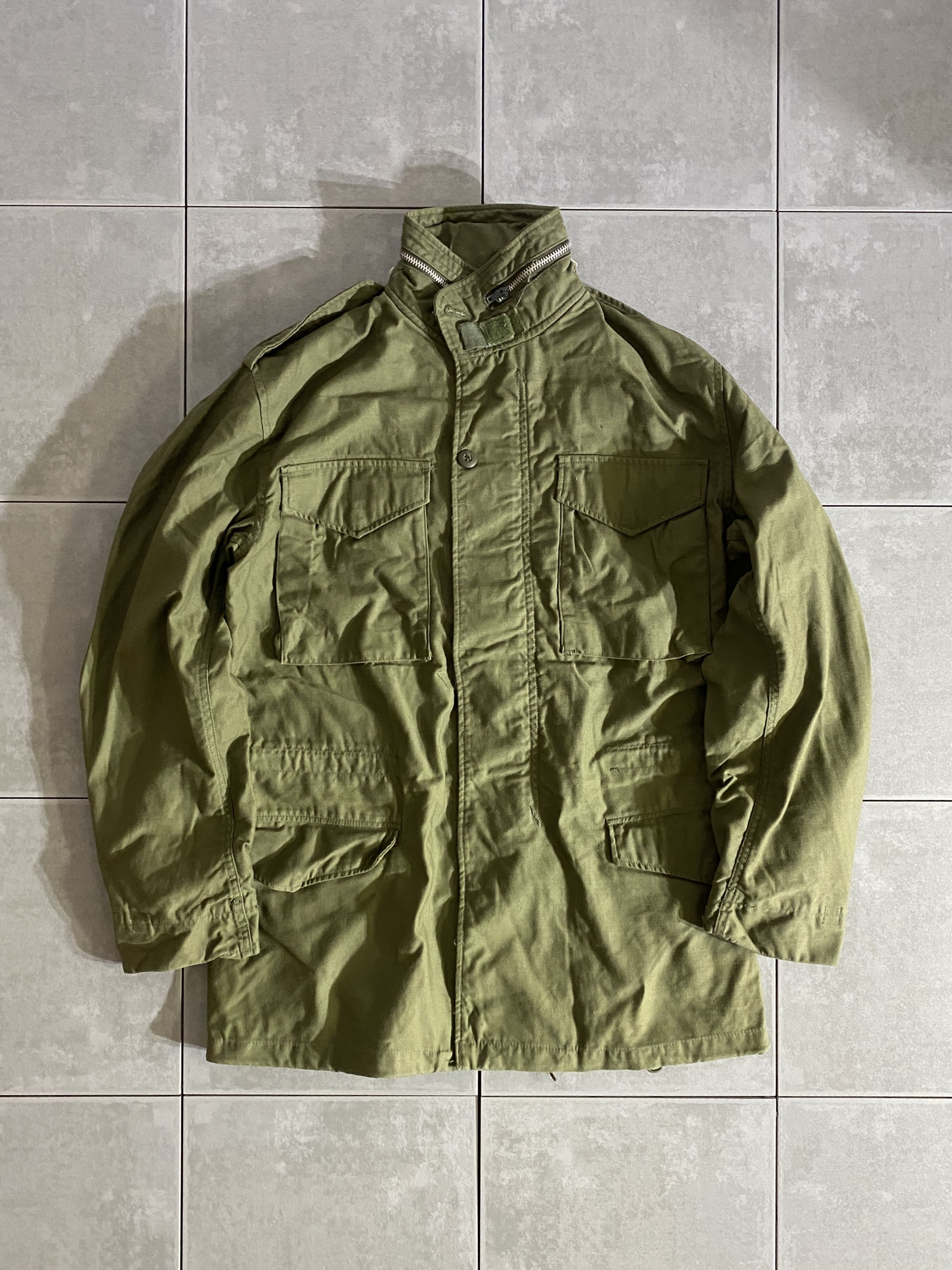 DEAD STOCK

70s M-65 FIELD JACKET 2nd Model

カラー：OD

サイズ：S-L
着丈：約80cm　身幅：約56cm　肩幅：約50cm　袖丈：約62cm

素材：コットン　ナイロン

米軍が開発したミリタリーアイテムの中で最高傑作ともいえる
M-65 FIELD JACKET。

ミリタリーを語る上で外せないアイテムです。

一般にファーストタイプ、アルミジッパータイプと呼ばれるのが、
この2nd Modelになります。

収納式フード、肩にはエポレット付きで
フロント部分はジッパーとスナップボタンで開閉できます。

ODのデッドストックはかなりレアで、
USEDでも放出がなく年々希少価値が上がっているので
今のうちに買っておくのがオススメです。

※画像の程度とは若干異なる場合がございますので予めご了承下さい。
(キズ、へこみ、汚れ、穴あき、ほつれ、文字書入れ(名前、ナンバー)など

