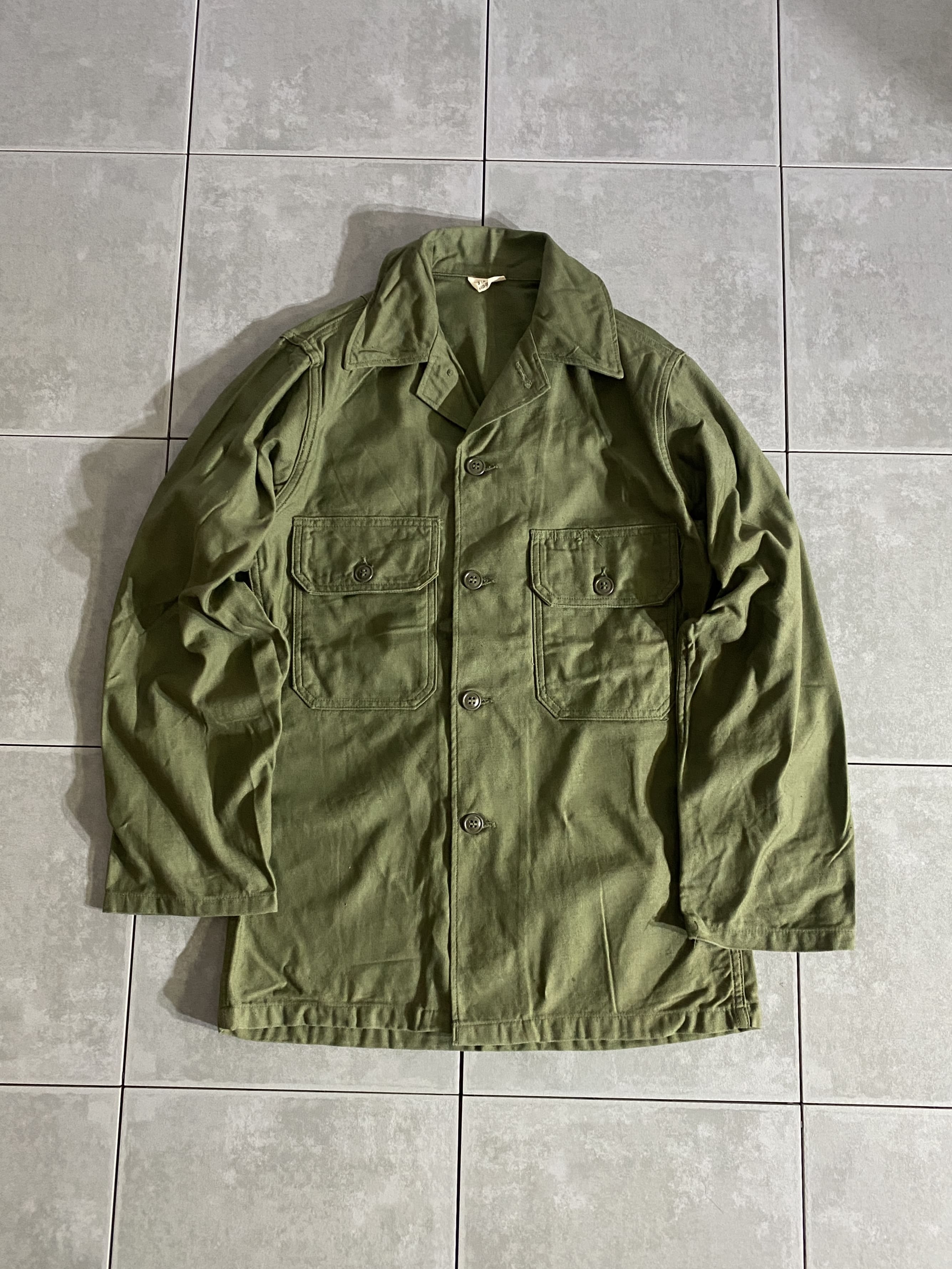 米軍放出品

60s Cotton Sateen Utility Shirt OG-107 2nd Model

カラー：OD

サイズ：13 1/2×31
着丈：約71cm　身幅：約50cm　肩幅：約40cm　袖丈：約58cm

素材：コットン

ミリタリーアイテムの中でも定番で人気のユーティリティシャツ。

1964年、筒袖タイプの2nd Modelになります。

このモデルの最大の特徴は袖口に調節用ストラップが
取り付けられています。

このストラップが兵士から不評だったのか
同年、数ヶ月間に発注されたコントラクトの物から
ストラップが外されています。

様々なタイプのあるユーティリティーシャツの中でも
市場では珍しく、希少性の高いアイテムかと思います。

コンディションも良く、まだまだ楽しんでお使いいただけます。

※画像の程度とは若干異なる場合がございますので予めご了承下さい。
(キズ、へこみ、汚れ、穴あき、ほつれ、文字書入れ(名前、ナンバー)など