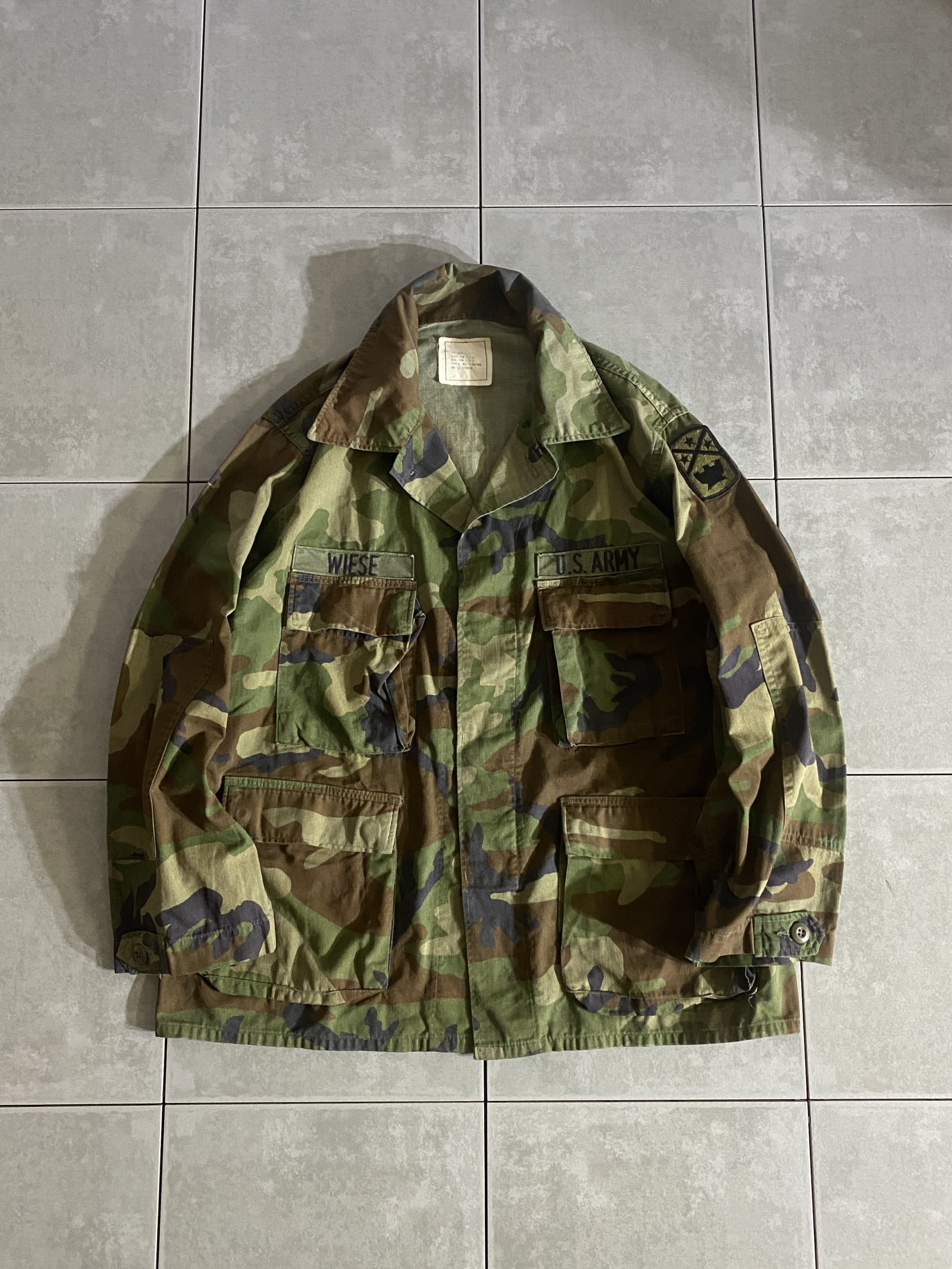 米軍放出品

80s BDU WOODLAND CAMO JACKET 前期型

カラー：WOODLAND

サイズ：L-S
着丈：約74cm　身幅：約64cm　肩幅：約50cm　袖丈：約62cm

素材：コットン50％　ナイロン50％

1981年より約30年以上にわたり全米軍で使用された
ウッドランドのBDUジャケット。

前期型は1981年から1984年頃まで生産されたモデルで、
胸ポケットのマチが内側に設けられており、
襟の形状が中期、後期と比較すると大きくなっております。

新品には出せない風合いのよい生地のアタリやムラ感は
USEDならではです。

年々希少価値が上がり、入手困難になっている
オススメアイテムの1つです。

※画像の程度とは若干異なる場合がございますので予めご了承下さい。
(キズ、へこみ、汚れ、穴あき、ほつれ、文字書入れ(名前、ナンバー)など