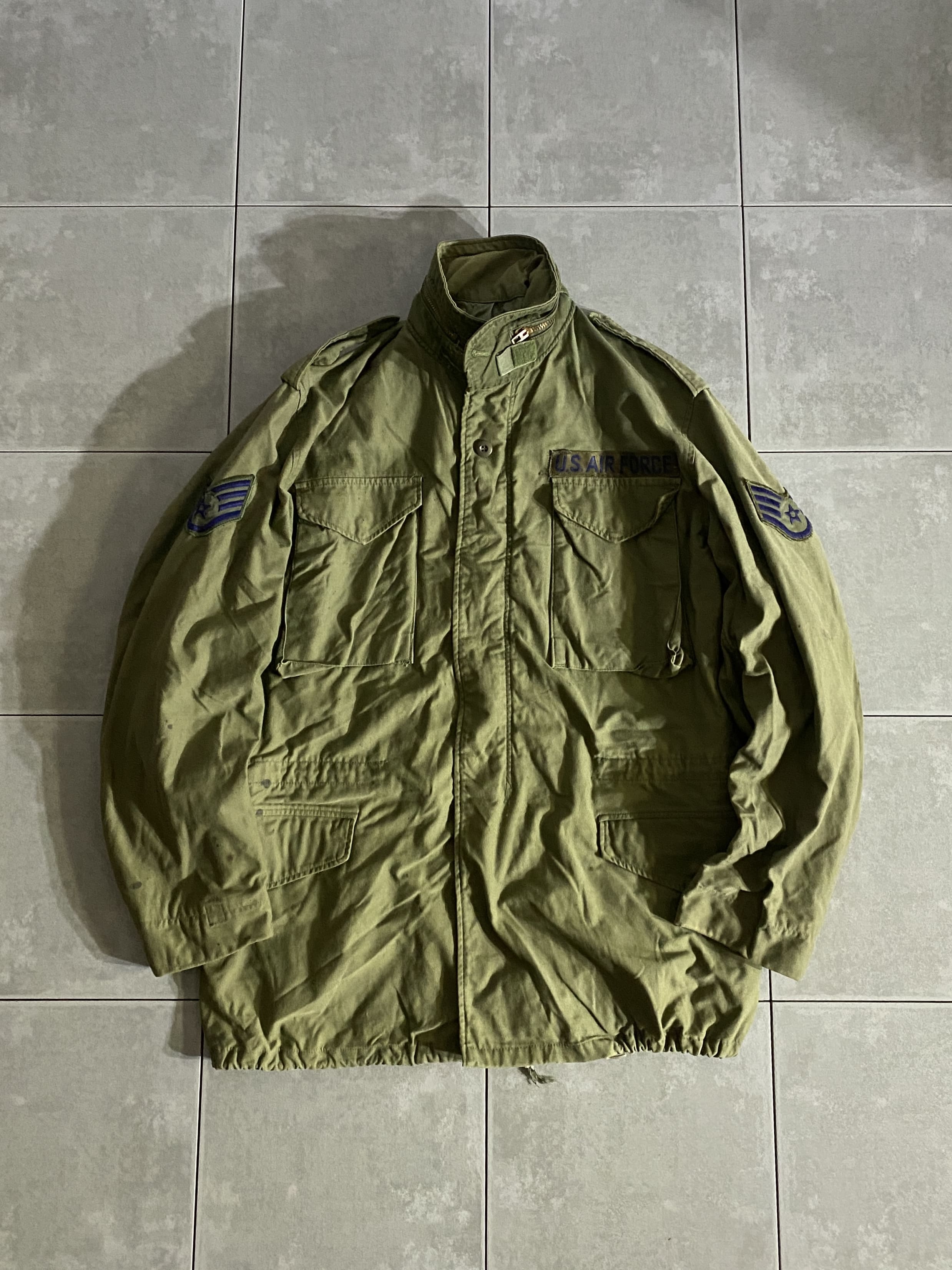 米軍放出品

70s M-65 FIELD JACKET 3rd Model

カラー：OD

サイズ：M-L
着丈：約83cm　身幅：約61cm　肩幅：約53cm　袖丈：約67cm

素材：コットン　ナイロン

GENERAL ZIP

軍が開発したミリタリーアイテムの中で最高傑作ともいえる
M-65 FIELD JACKET。

ミリタリーを語る上で外せないアイテムです。

アルミジップからブラスジップに変わった
3rd Model。

収納式フード、肩にはエポレット付きで
フロント部分はジッパーとスナップボタンで開閉できます。

目立ったダメージもないグッドコンディションです。

ODは特に放出がなく年々希少価値が上がっているので
今のうちに買っておくのがオススメです。

※画像の程度とは若干異なる場合がございますので予めご了承下さい。
(キズ、へこみ、汚れ、穴あき、ほつれ、文字書入れ(名前、ナンバー)など
