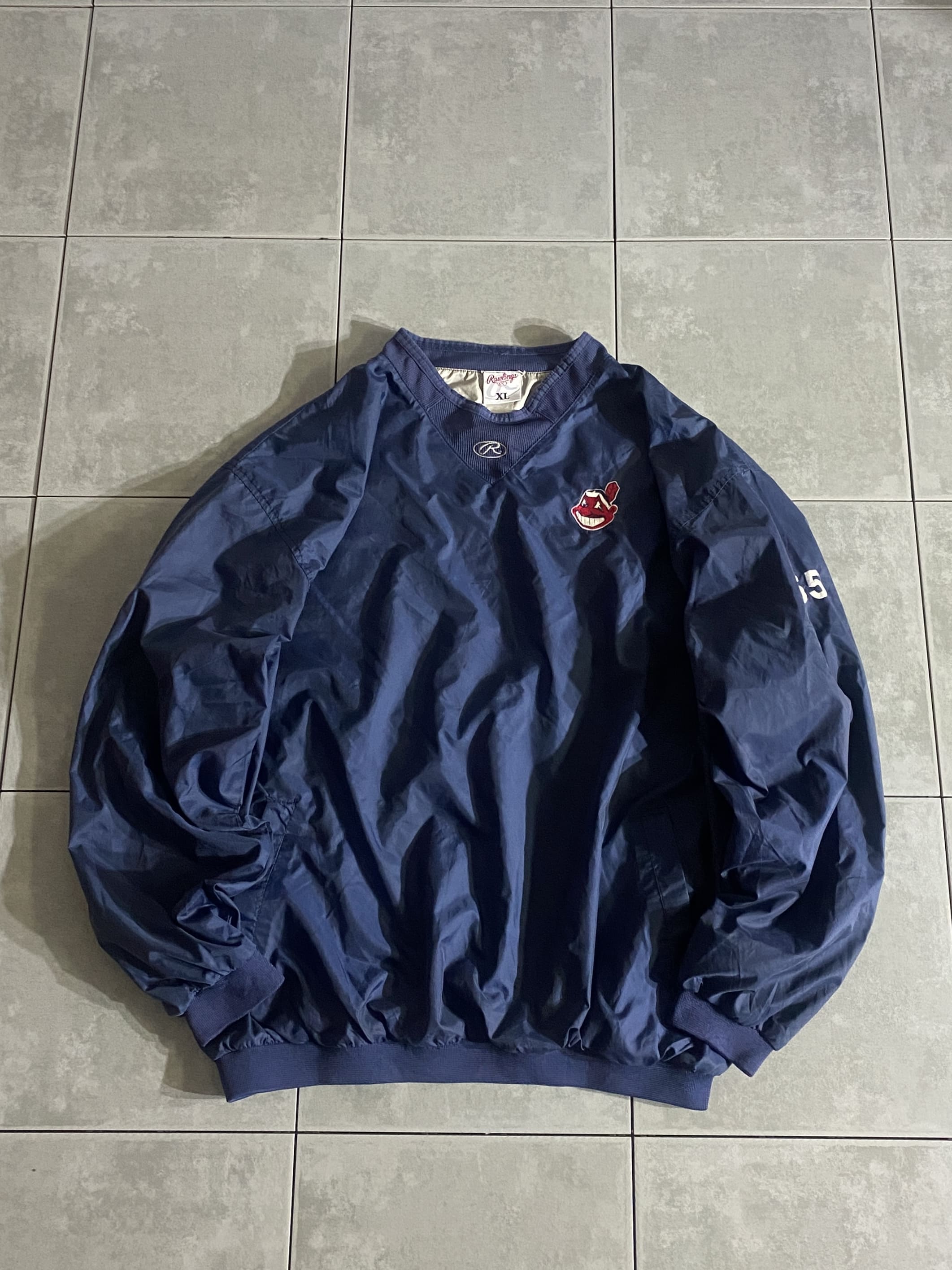 Rawlings

【Rawlings】MLB Cleveland Indians Pullover Nylon Jacket 

【カラー】ネイビー

【サイズ】XL
着丈：約73cm　身幅：約71cm　肩幅：約61cm　袖丈：約63cm

【素材】ナイロン

Rawlingsのプルオーバーナイロンジャケット。

1887年設立のRawlings。

張りのあるノンリップナイロン素材に
合わせやすいネイビーカラー。

左胸には、廃盤となったワフー酋長のロゴパッチ。

一枚着はもちろん、インナーにパーカー仕込んだり、
運動時に着用したりと様々なスタイリングが楽しめるアイテムです。

※画像の程度とは若干異なる場合がございますので予めご了承下さい。
(キズ、へこみ、汚れ、穴あき、ほつれ、文字書入れ(名前、ナンバー)など