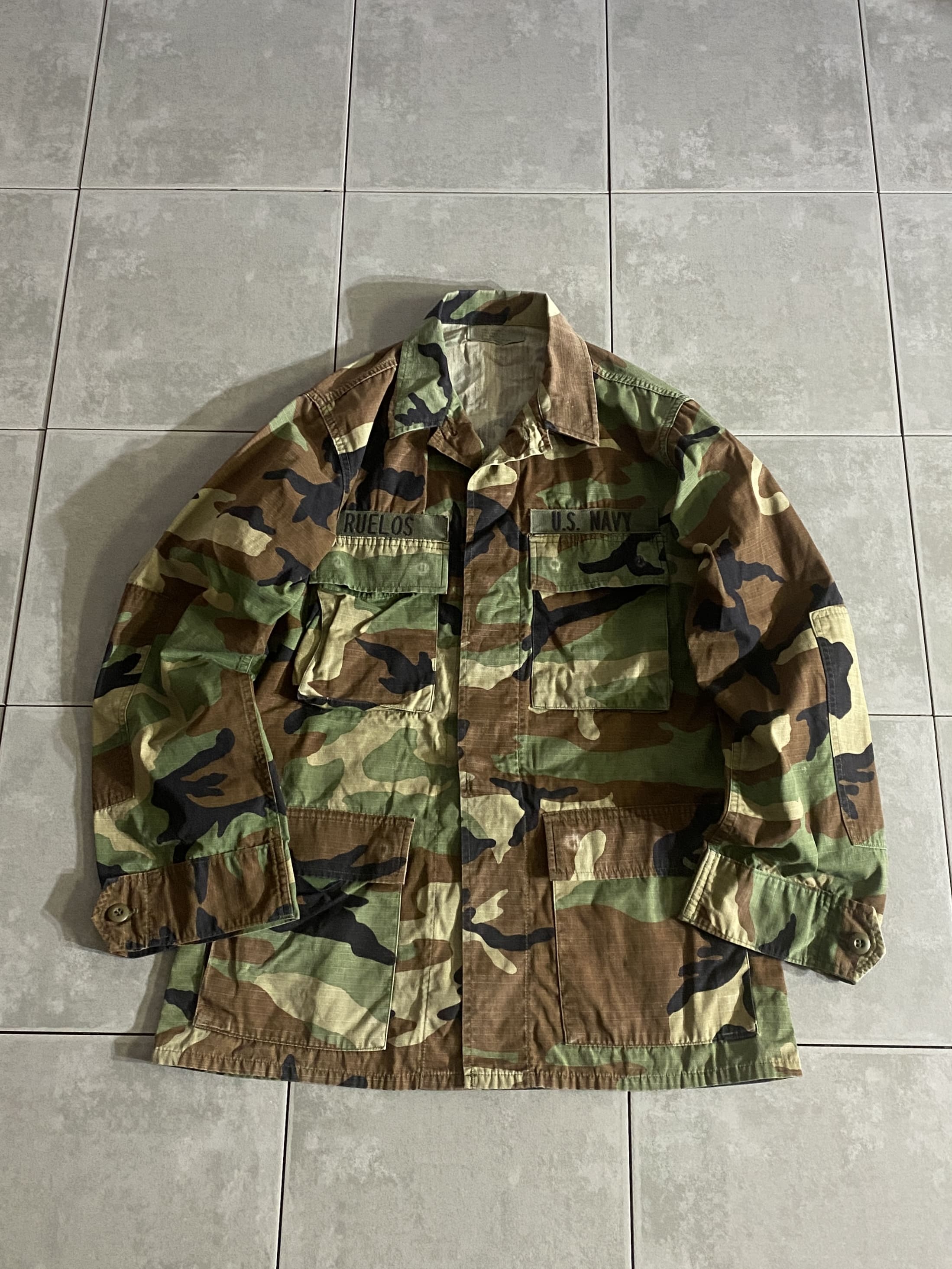 米軍放出品

HOT WEATHER BDU JACKET

【カラー】WOODLAND

【サイズ】S-R
着丈：約78cm　身幅：約57cm　肩幅：約45cm　袖丈：約62cm

【素材】コットン50％　ナイロン50％

リップストップ生地

ウッドランドのHOT WEATHER BDUジャケット。

広範な気候と温度に対応するように開発された
薄手生地のジャケットです。

フロントに4つのポケットがございます。

シャツジャケットのような感覚で、
真冬以外の3シーズン着用いただけます。

※フラップポケット4つとも全てのボタン外されております。

※画像の程度とは若干異なる場合がございますので予めご了承下さい。
(キズ、へこみ、汚れ、穴あき、ほつれ、文字書入れ(名前、ナンバー)など