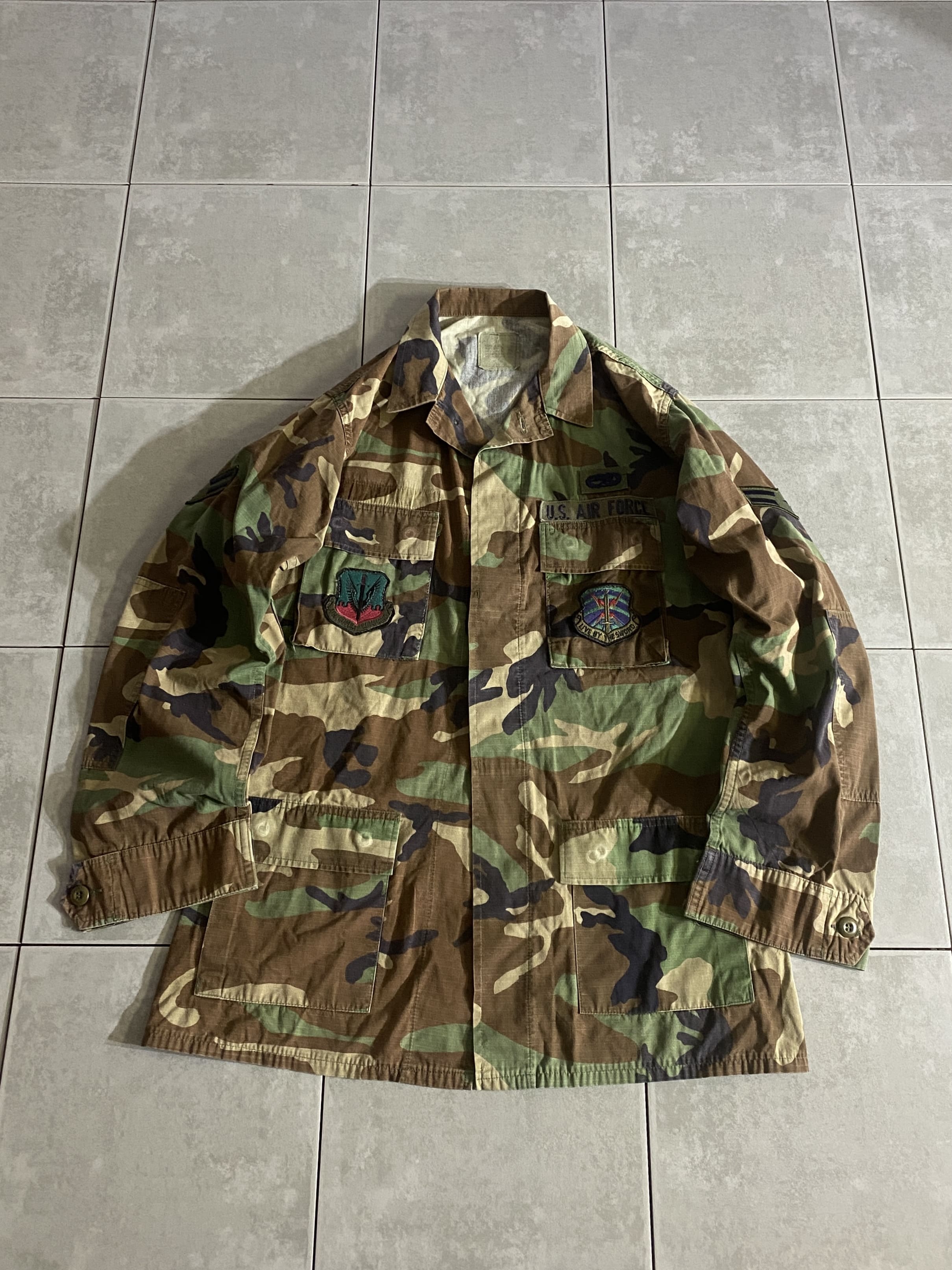 米軍放出品

HOT WEATHER BDU JACKET

【カラー】WOODLAND

【サイズ】M-XL
着丈：約82cm　身幅：約60cm　肩幅：約47cm　袖丈：約67cm

【素材】コットン50％　ナイロン50％

リップストップ生地

ウッドランドのHOT WEATHER BDUジャケット。

広範な気候と温度に対応するように開発された
薄手生地のジャケットです。

フロントに4つのポケット、階級章などのパッチが
付いております。

シャツジャケットのような感覚で、
真冬以外の3シーズン着用いただけます。

※画像の程度とは若干異なる場合がございますので予めご了承下さい。
(キズ、へこみ、汚れ、穴あき、ほつれ、文字書入れ(名前、ナンバー)など