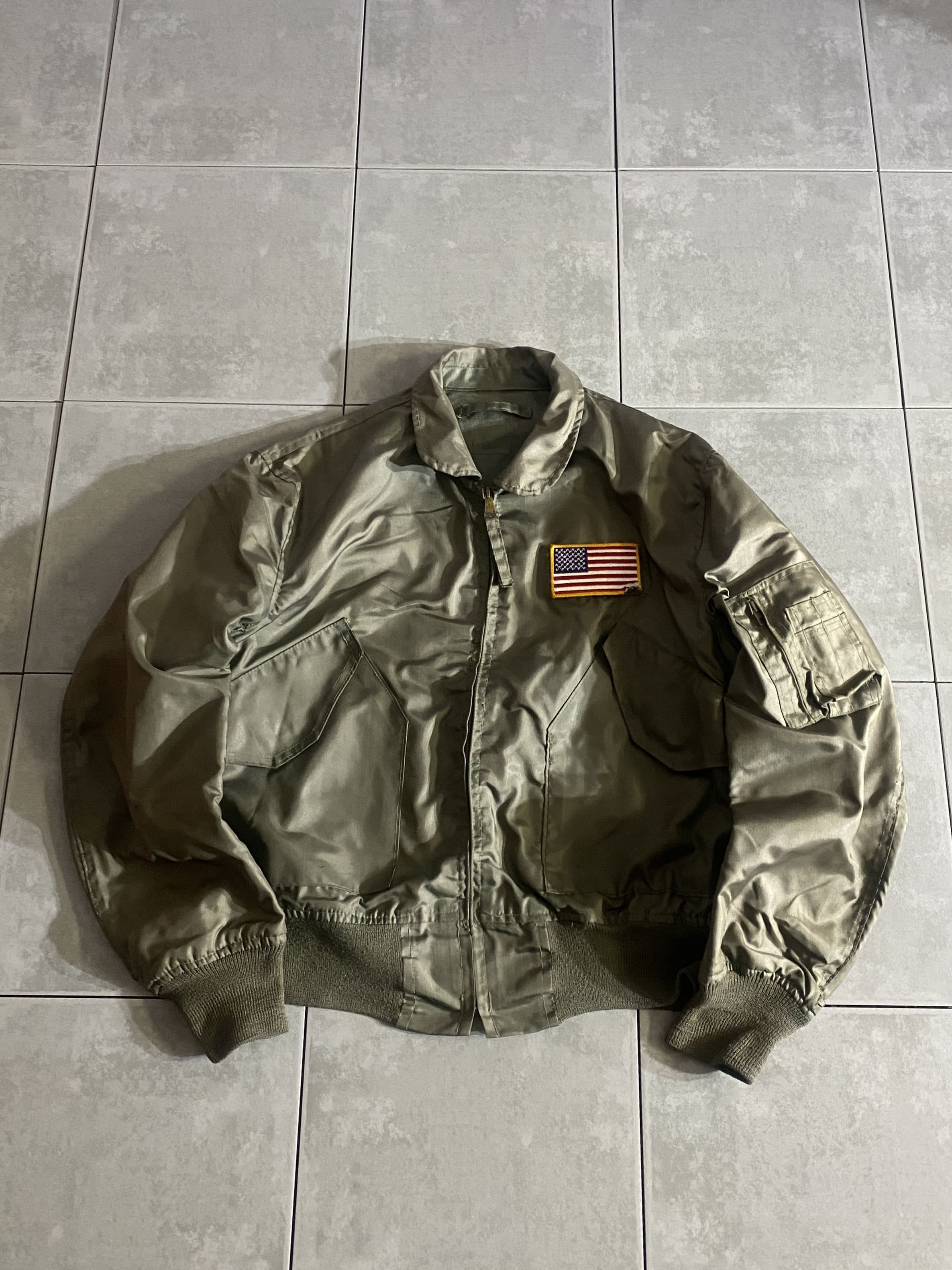 米軍放出品

CWU-36/P Flight Jacket

【カラー】SAGE

【サイズ】不明
着丈：約64cm　身幅：約54cm　肩幅：約51cm　袖丈：約65cm

【素材】アラミド100％

ZIP SCOVILL社製

米軍実物のCWU-36/P フライトジャケット。

昨今、希少価値も上がり価格も高騰している実物品。

古着屋などでも中々見かけないアイテムで、
レプリカとは一味も二味も違う雰囲気が漂っています。

目立ったダメージもないグッドコンディションです。

※星条旗のパッチは破れがございます。

※タグ、切り取られています。

※画像の程度とは若干異なる場合がございますので予めご了承下さい。
(キズ、へこみ、汚れ、穴あき、ほつれ、文字書入れ(名前、ナンバー)など
