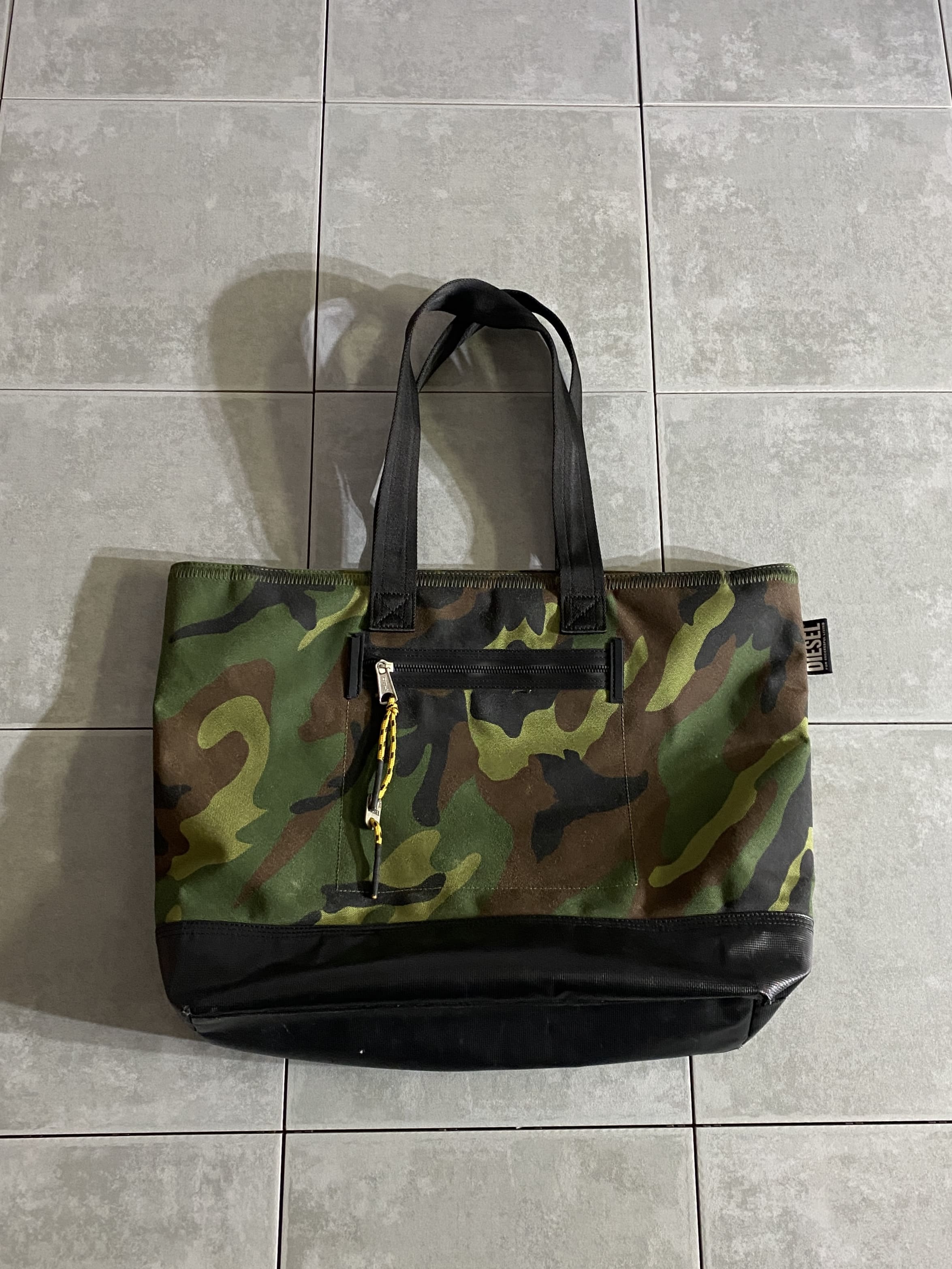 DIESEL

【DIESEL】Tote Bag

【カラー】Woodland/Multicam

【サイズ】約39×50×15cm

【素材】ポリエステル89％　ポリ塩化ビニル11％

フロントとバックのデザインが異なるDIESELらしい
遊び心のあるミリタリートートバッグ。

軽量で丈夫な生地を使用し収納力も抜群。

細部にまでこだわったデザインや存在感がGood。

ジッパー付きなので、旅行などにもオススメです。

※画像の程度とは若干異なる場合がございますので予めご了承下さい。
(キズ、へこみ、汚れ、穴あき、ほつれ、文字書入れ(名前、ナンバー)など