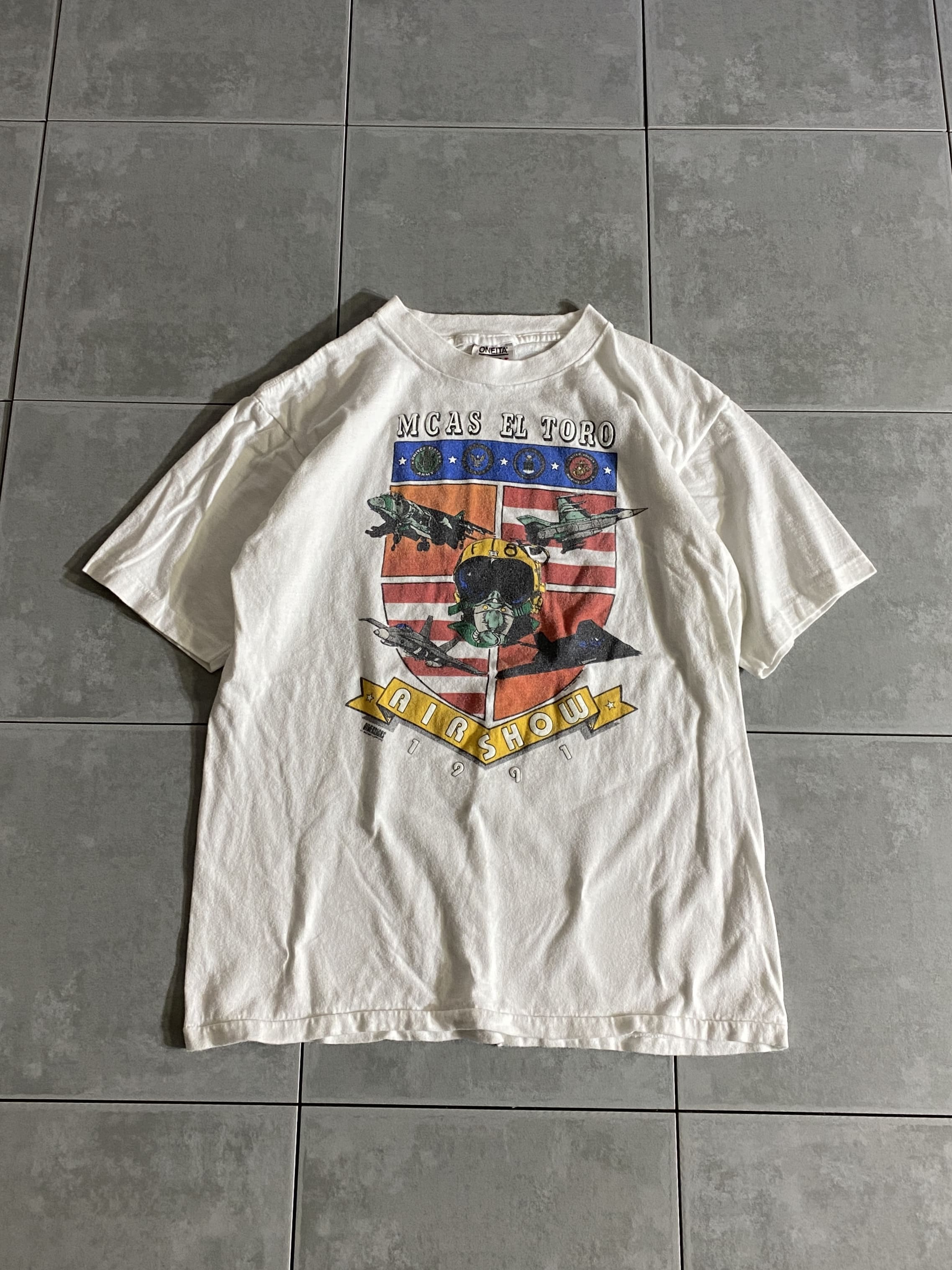 ONEITA

【ONEITA】90s AIR SHOW 1991 S/S Tee Made in USA

【カラー】ホワイト

【サイズ】L
着丈：約62cm　身幅：約48cm　肩幅：約46cm　袖丈：約20cm

【素材】コットン100％

1991年に開催されたAIR SHOWの
販促用Tシャツかと思われます。

ボディーはONEITAのUSA製。

デザイン性の高さと配色の良さが際立つ
手の込んだ1着となっております。

※フロント、バックの左右脇部分シミがございます。

※画像の程度とは若干異なる場合がございますので予めご了承下さい。
(キズ、へこみ、汚れ、穴あき、ほつれ、文字書入れ(名前、ナンバー)など

